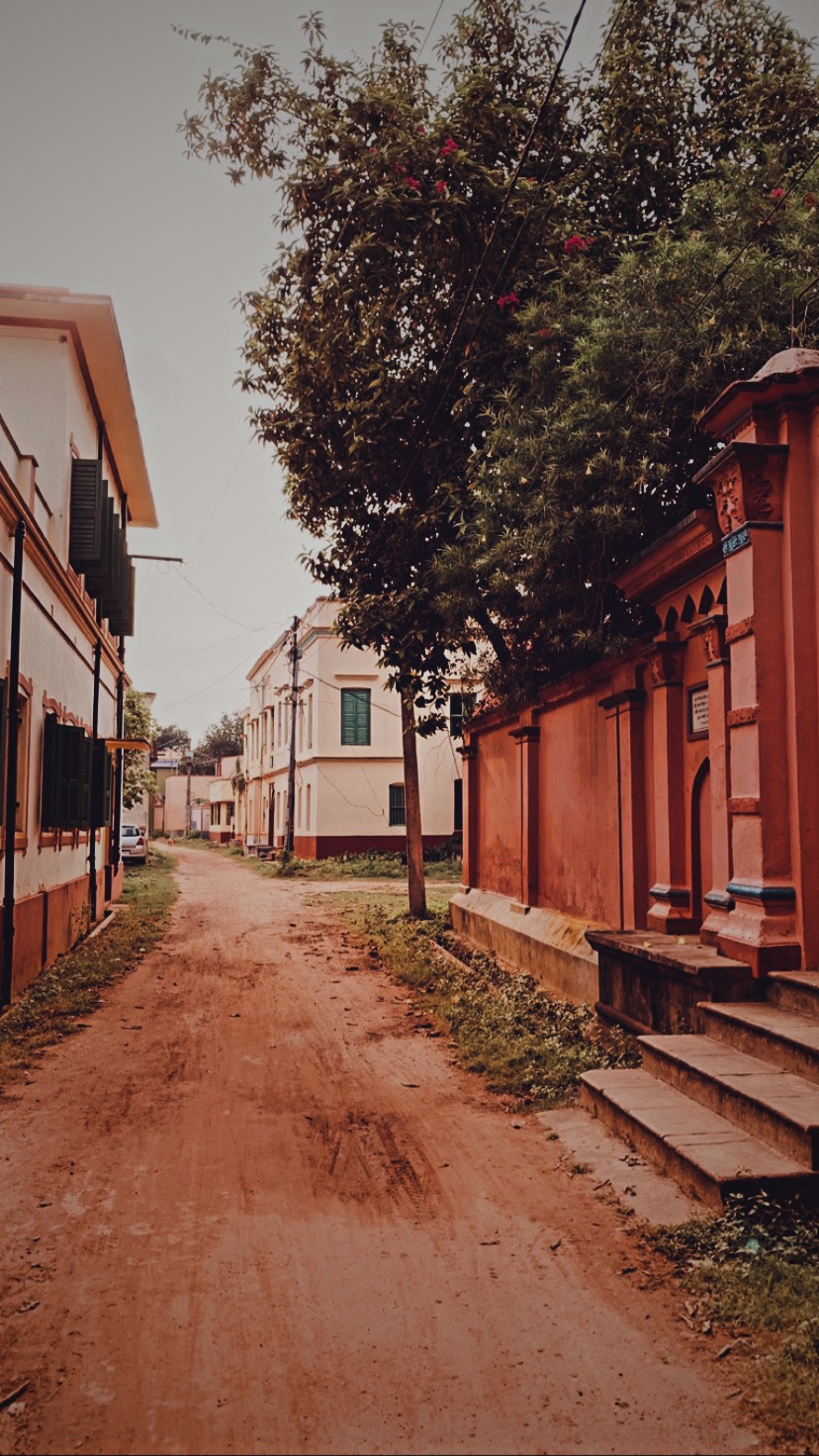 A red-earth village lane beside the Chaudhuri mansion at Amadpur